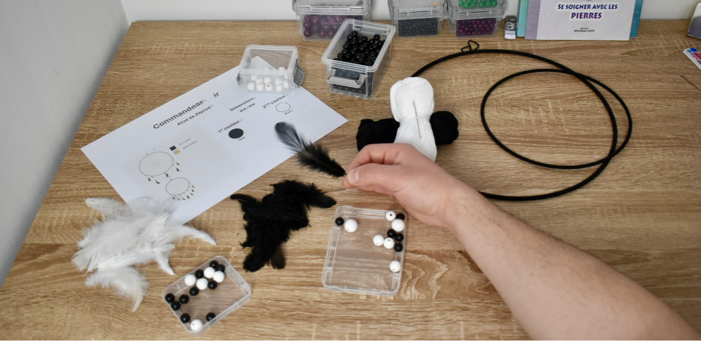 Matériaux pour attrape-rêve Zéphir : cercles noirs, fils blanc et noir, perles et plumes assorties sur plan de travail.
