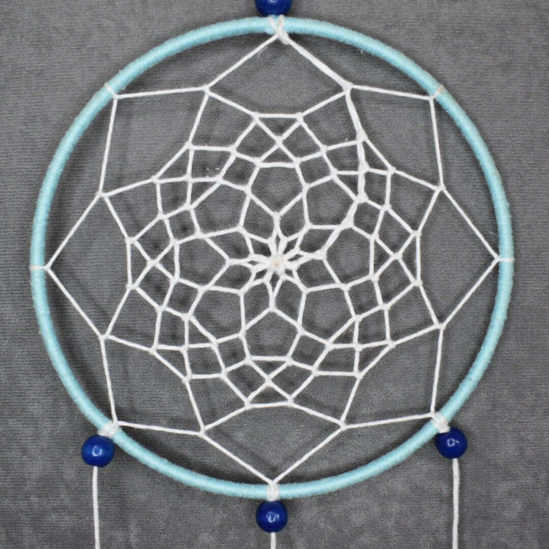 Détail du tissage étoile à 8 branches style fleur de lotus, fil bleu ciel et blanc, perles bois bleu, plumes assorties.
