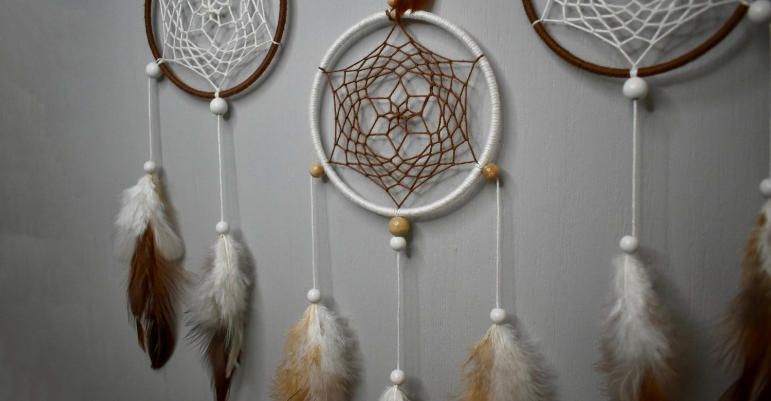 Gros plan sur trois cercles tissés brun et blanc avec perles bois clair et plumes naturelles.